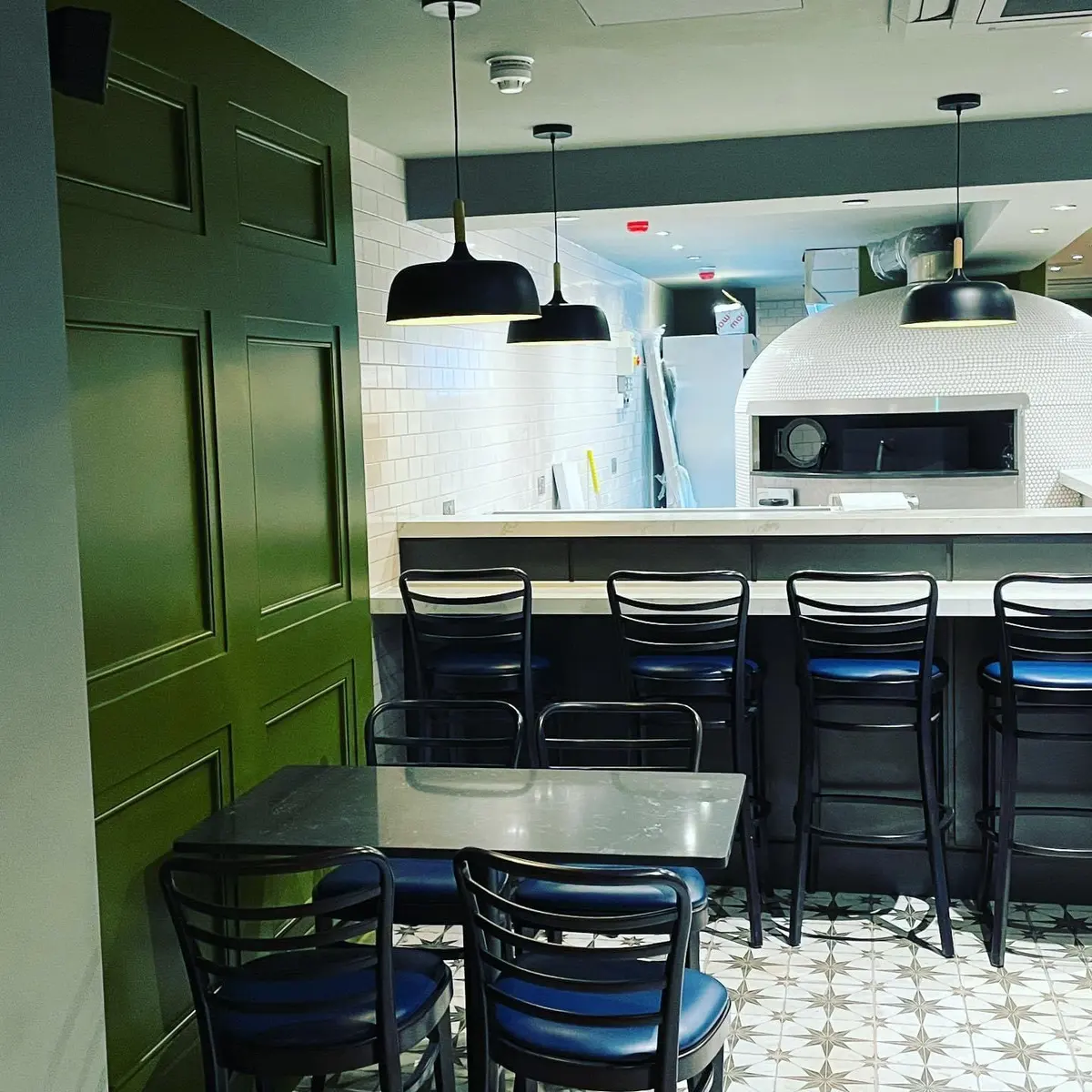 Cafe fit-out with green panelled door, bar seating and a pizza oven